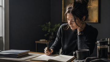 Woman resting her head on her hand while writing notes at a desk, for an article on nootropic ingredients for perimenopause